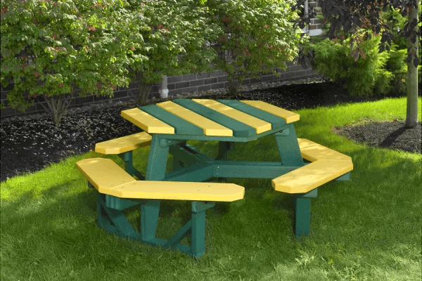 Green and yellow hexagonal picnic table on grass, surrounded by lush greenery.